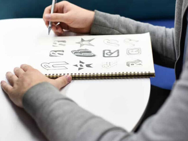 hand-holding-notebook-with-drew-brand-logo-P8HTW8W-1200×600 An artist drawing different brand logos