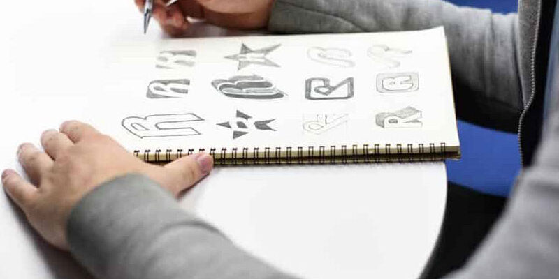 hand-holding-notebook-with-drew-brand-logo-P8HTW8W-1200×600 An artist drawing different brand logos