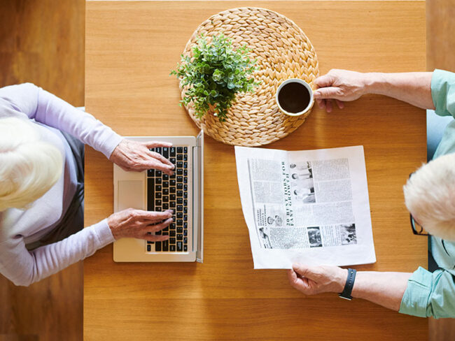 overview-of-senior-husband-with-newspaper-and-wife-T9ANDFP