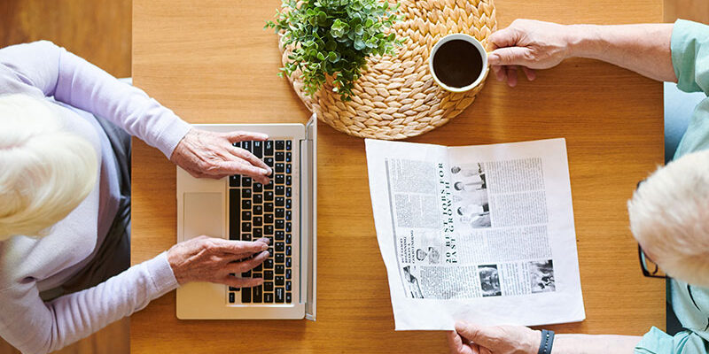 overview-of-senior-husband-with-newspaper-and-wife-T9ANDFP