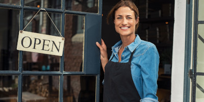 A woman smiling in a doorway of a business with an open sign hung up