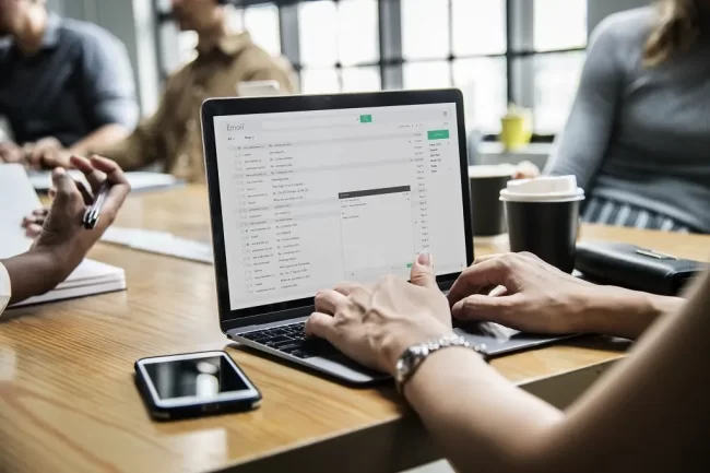 woman-checking-her-email-in-a-meeting Woman in a business meeting drafts an email on a laptop.