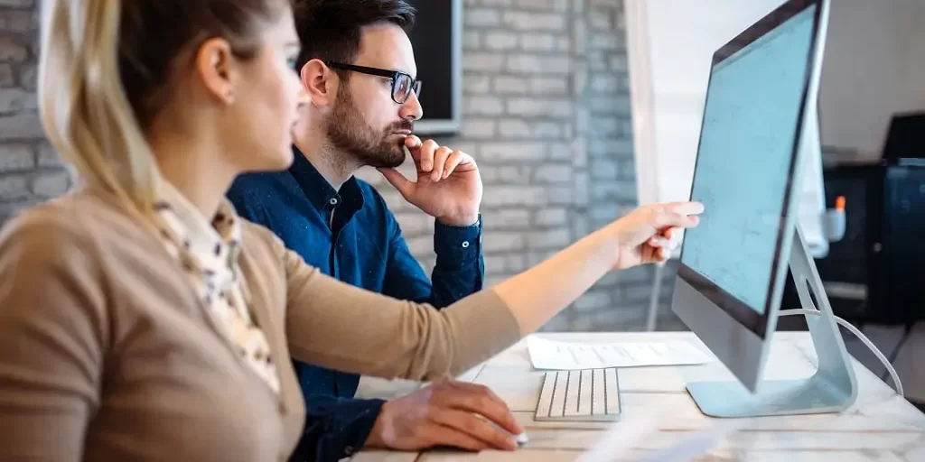 software-engineers-working-on-project-2023-11-27-05-13-43-utc-min A woman points to the screen of a computer that a man works at in a modern office setting.