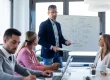 A businessman explains an SEO project to his team on a white board in a meeting space.